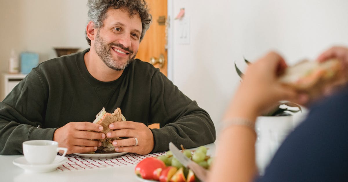 Why does my bread ferment in the middle? - Smiling middle aged guy with beard and gray hair in casual wear eating toast while having breakfast with wife in kitchen Why does my bread ferment in the middle? - Smiling middle aged guy with beard and gray hair in casual wear eating toast while having breakfast with wife in kitchen