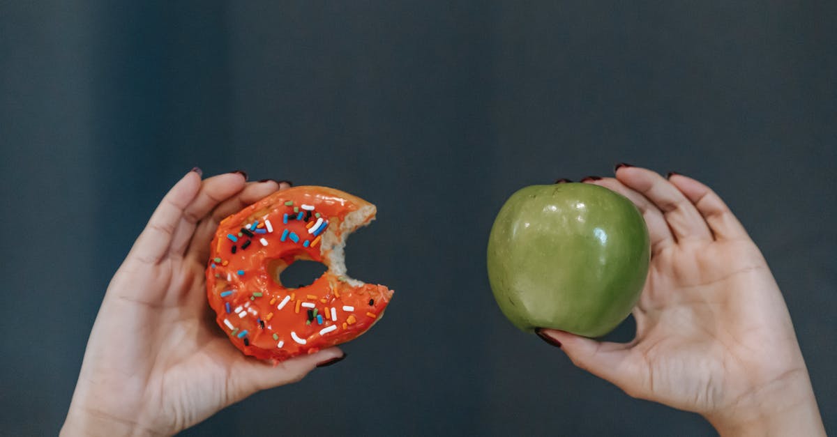 Why does my glaze soak into my doughnuts? - Crop unrecognizable young female demonstrating bitten high calorie doughnut and healthy green apple against gray background Why does my glaze soak into my doughnuts? - Crop unrecognizable young female demonstrating bitten high calorie doughnut and healthy green apple against gray background