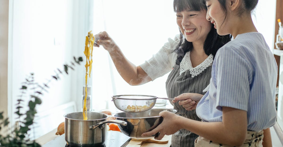 Why drain soaked rice? - Side view of smiling Asian teenager with middle age mother serving hot boiled pasta in drainer Why drain soaked rice? - Side view of smiling Asian teenager with middle age mother serving hot boiled pasta in drainer