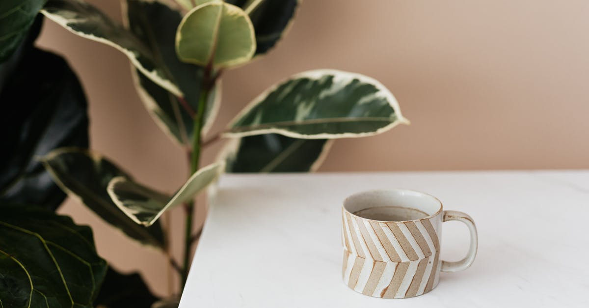 Why is my green tea brown? - Brown and white striped ceramic cup of coffee placed on white marble table near big green ficus plant Why is my green tea brown? - Brown and white striped ceramic cup of coffee placed on white marble table near big green ficus plant