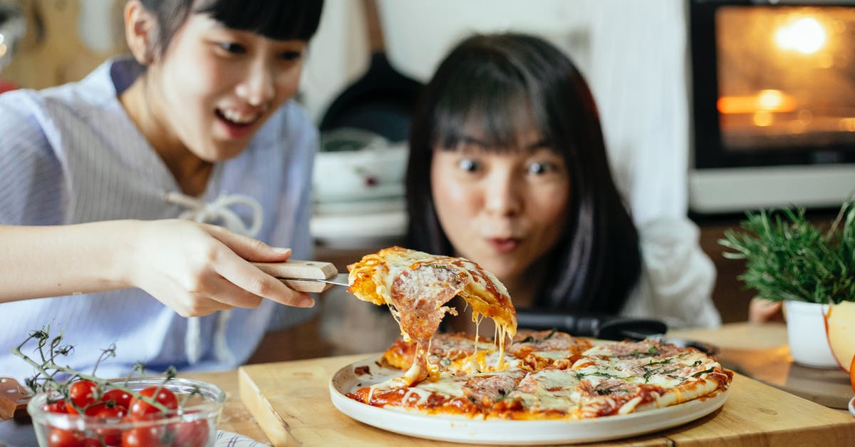 Why is this (and other?) pizza oven so unnecessarily tall? - Crop delightful Asian ladies smiling while cutting piece of delicious homemade pizza with stretched cheese on cutting board in kitchen