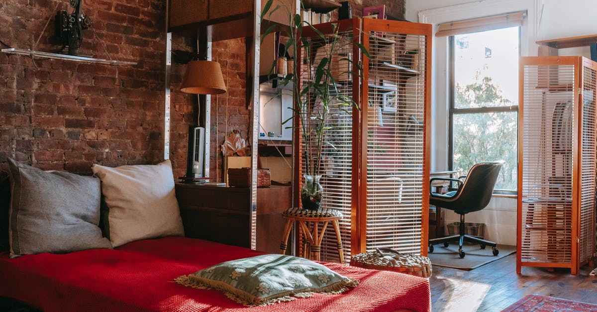Why not cover the pot? - Comfortable bed with red cover and pillows placed near brick wall in cozy room with isolated workspace decorated with houseplants near window Why not cover the pot? - Comfortable bed with red cover and pillows placed near brick wall in cozy room with isolated workspace decorated with houseplants near window