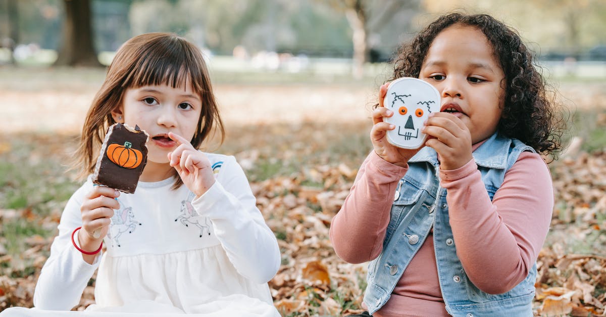 Why should I rest gingerbread dough? - Adorable little multiethnic girls in casual outfits sitting on ground in park with sweets decorated for Halloween Why should I rest gingerbread dough? - Adorable little multiethnic girls in casual outfits sitting on ground in park with sweets decorated for Halloween