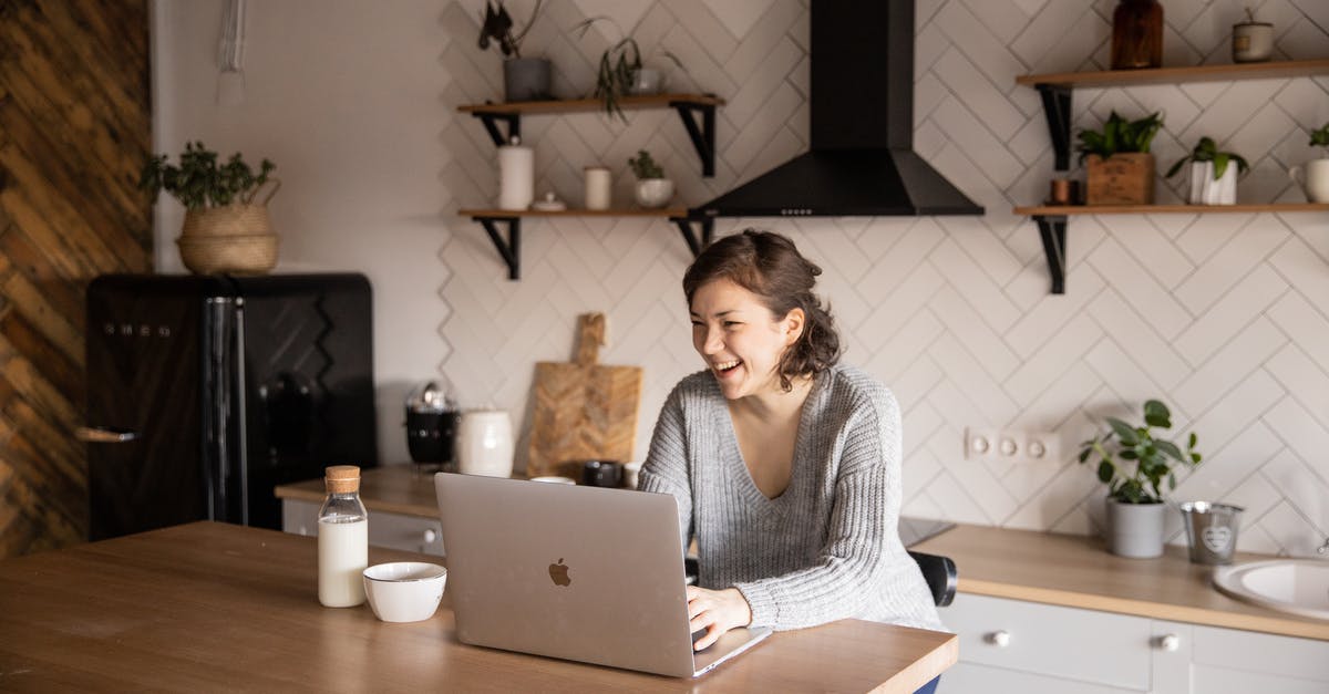 Why use milk in scrambled eggs? - Young female in gray sweater laughing while sitting at wooden table with laptop and milk bottle and having rest watching video during free time