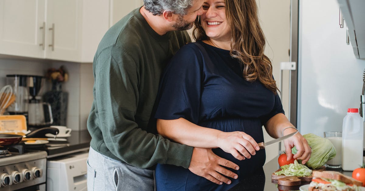Why wait for some hours before filling any food into a new freezer? - Cheerful pregnant wife in blue dress cooking sandwiches for breakfast while smiling and looking at husband embracing belly in modern kitchen