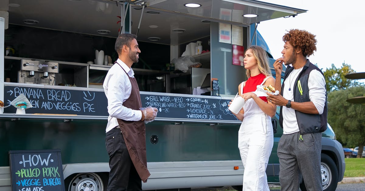 Would it be advisable to partially pre-grill hamburgers and freeze so that they can be pan fried when a customer orders? - Side view of happy young ethnic waiter in uniform standing near food van and smiling while greeting diverse customers eating delicious takeaway burger and french fries