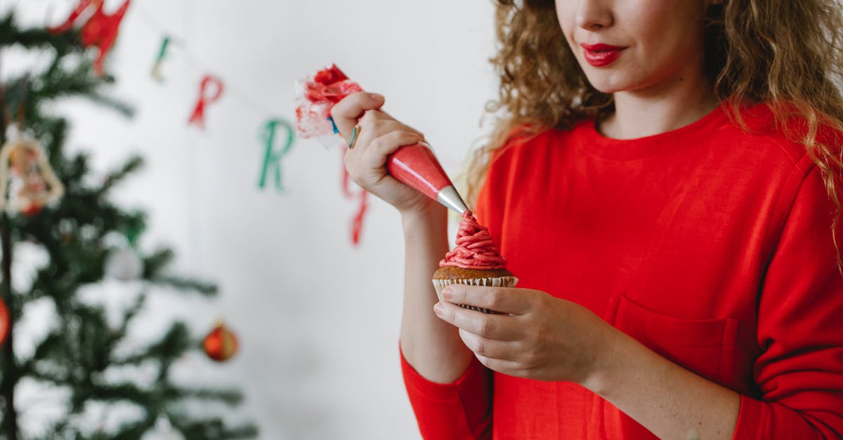 Xmas Pudding put in microwave by mistake for 5 minutes - Concentrated young lady in red sweater piping red cream on cupcake with pastry bag in light room with white wall and decorated Christmas tree Xmas Pudding put in microwave by mistake for 5 minutes - Concentrated young lady in red sweater piping red cream on cupcake with pastry bag in light room with white wall and decorated Christmas tree