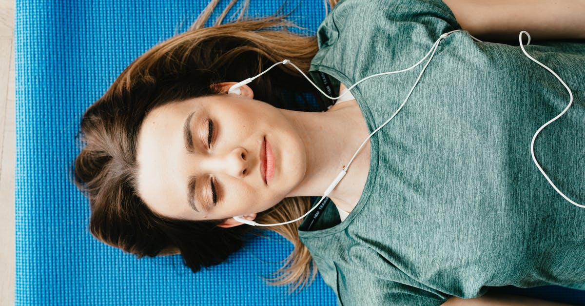 Yolks flat and breaking - Tranquil woman resting on yoga mat in earphones at home Yolks flat and breaking - Tranquil woman resting on yoga mat in earphones at home